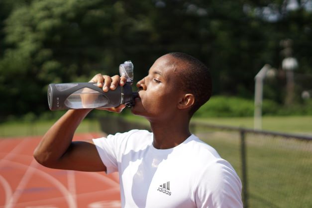 Běžec tmavé pleti má pauzu na tréninku a pije vodu z průhledného shakeru